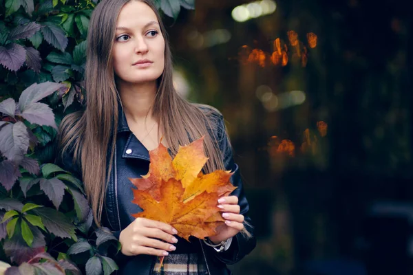 Jovem mulher com folhas de outono na mão e queda amarelo bordo jardim fundo — Fotografia de Stock