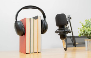 Profesyonel bir mikrofon, kayıt ve yayın için kitap ve kulaklık ile ayakta duruyor. Podcast konsepti.