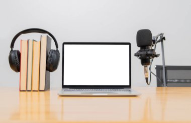 Profesyonel podcast mikrofon ve dizüstü bilgisayar. Ekran, kulaklık, ahşap masa üzerinde kitaplar. Boşluğu kopyala.
