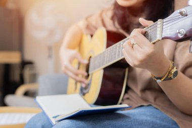 Şarkıcı söz yazarı konforlu bir evde müzik bestelerken gitar çalıyor. Müzikal ilham konsepti. Seçici odak.