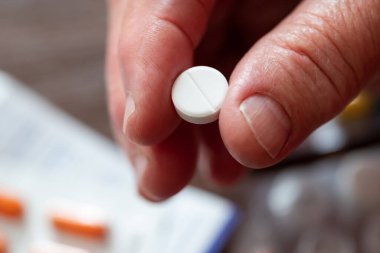 Elinde beyaz bir hap tutan yaşlı bir kadın. Beyaz, yuvarlak bir hap tutan bir emeklinin yakın çekimi, alınmaya hazır.