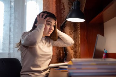 Ödevinin yoğunluğundan dolayı umutsuzluğa düşmüş bir öğrenci. Bir kız dizüstü bilgisayara bakarken başını tutarak ödevlerin miktarına ve egzersizlerin zorluğuna şaşırır.