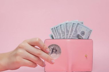 Üzerinde dolar olan pembe cüzdan ve fotokopi alanı olan pembe arka planda kadının elinde bitcoin..