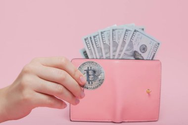 Üzerinde dolar olan pembe cüzdan ve fotokopi alanı olan pembe arka planda kadının elinde bitcoin..