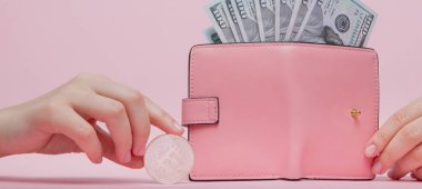 Üzerinde dolar olan pembe cüzdan ve fotokopi alanı olan pembe arka planda kadının elinde bitcoin..