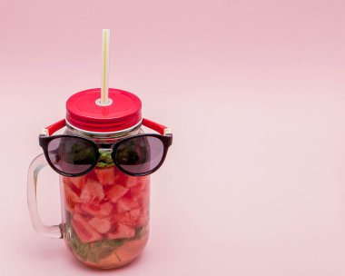 Dilim karpuz ve pembe bir arka plan üzerinde buz ile soğuk taze limonata bir kavanoz yatarken gözlük