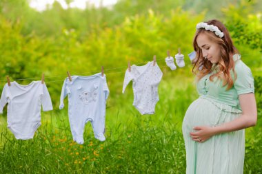 Güzel hamile kadın dışarıda çocuk kıyafetlerini asıyor. Harika zamanlama..