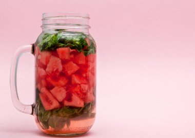 Kavanoz dilim karpuz ve pembe bir arka plan üzerinde buz ile soğuk taze limonata.