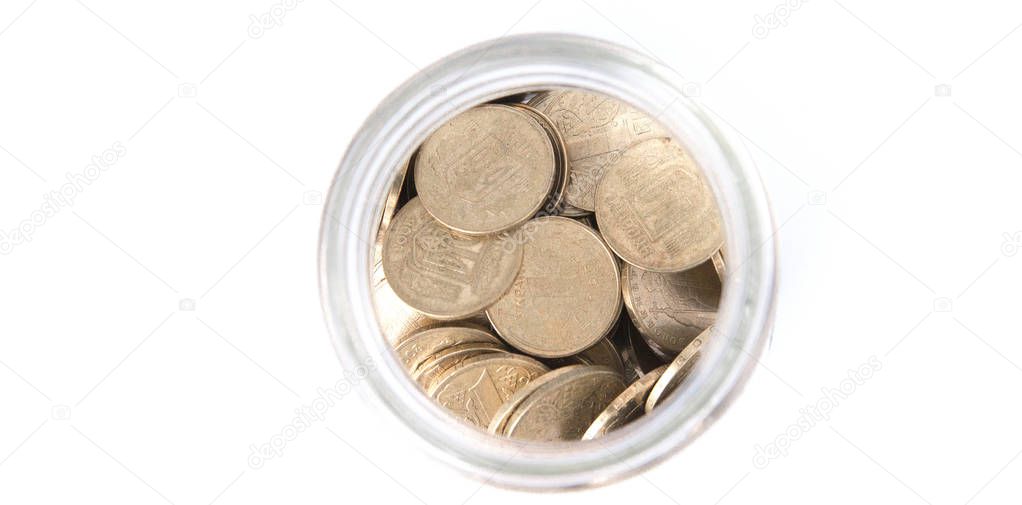 Close up coins in glass jar on white table. Coins scattered around. Isolated on white background.