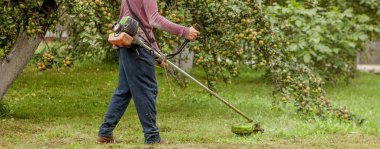 Makine kullanarak bahçıvan bahçe yeşil çim kesme. Bahçe Ekipmanları. Genç adam bir düzeltici ile çim biçme