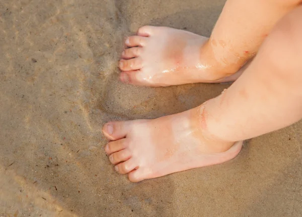 Bebé pequeño dando sus primeros pasos en la playa. Bebé de pies desnudos que permanece en la arena cerca de la orilla en el día soleado. Concepto de vacaciones de verano. Vista superior. Copiar espacio — Foto de Stock