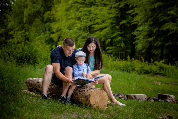 Mãe feliz, pai e filho lêem um livro no parque — Fotografia de Stock