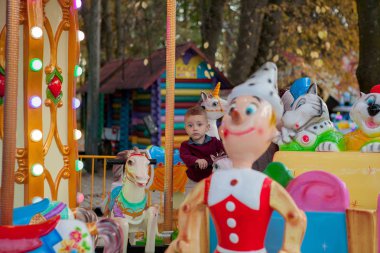 ata binme küçük komik lunaparktaki dolambaçlı bir atlıkarınca bir çocuktur. Mutlu çocuk, güneşli bir günde dışarıda eğleniyor.