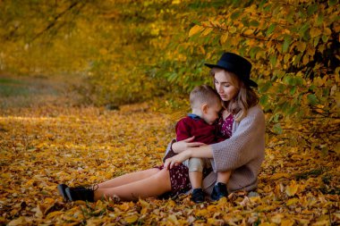 Mutlu genç anne ile bebek ile sarı Akçaağaç Sonbahar parkta oynarken bırakır. Aile açık havada yürüyüş sonbaharda. Sonbaharda parkta oynarken annesi ile küçük çocuk