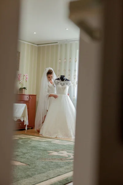 A noiva encantadora com damas de honra fica perto do vestido de noiva. Preparação da manhã do casamento nupcial — Fotografia de Stock