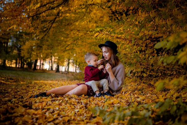 黄色のもみじで秋の公園で赤ちゃんと遊んで幸せな若い母を残します 秋の野外を歩いている家族 秋の公園で遊ぶ母親と少年 — ストック写真