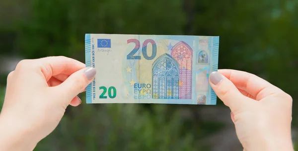 Hands holding 20 euro banknote on the green background. Check euro for authenticity.