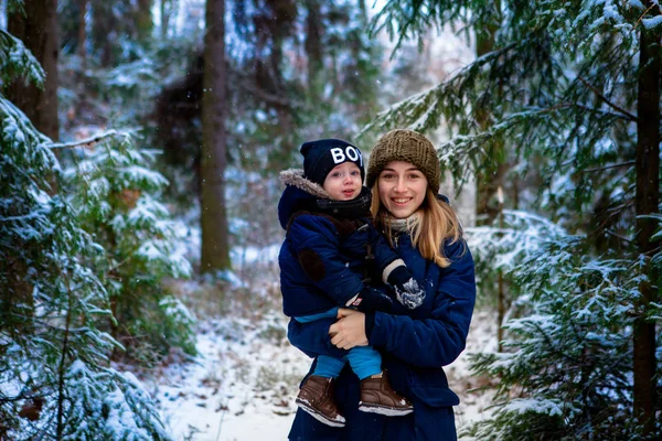 Mutter hält ein kleines Kind in den Armen. ein Spaziergang im verschneiten Winterpark. — Stockfoto