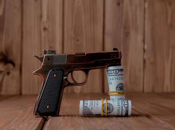 Robbery concept. Gun with money on wooden background.