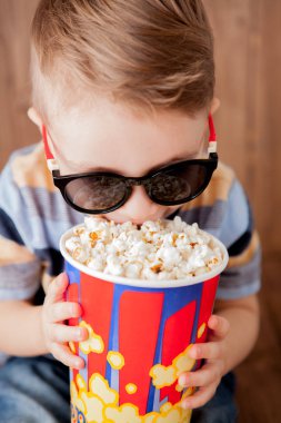 Küçük şirin çocuk bebek çocuk 2-3 yaşında, patlamış mısır, ahşap arka plan üzerinde hızlı yemek yeme için kova tutarak 3d IMAX sinema gözlük. Çocuklar çocukluk yaşam tarzı kavramı. Kopya alanı.