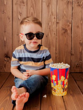 Küçük şirin çocuk bebek çocuk 2-3 yaşında, patlamış mısır, ahşap arka plan üzerinde hızlı yemek yeme için kova tutarak 3d IMAX sinema gözlük. Çocuklar çocukluk yaşam tarzı kavramı. Kopya alanı.