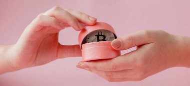 Pembe bir arka plan, sanal para simgesi pembe hediye kutusunda Bitcoin holding kadının eller.