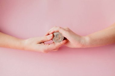 Sanal paranın sembolü olan pembe arka planda Bitcoin tutan kadının elleri.