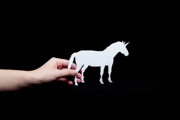 A woman's hand holds a white unicorn with a black background paper.