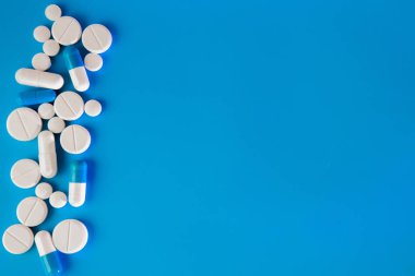 Mavi masaya saçılmış beyaz haplar. Reklam, web geçmişi ya da diğer fikirler için özel teklifler alın. Tıbbi, eczane ve sağlık hizmetleri konsepti. Uzayı kopyala Metin veya logo için boş yer.