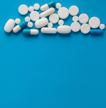 Mavi masaya saçılmış beyaz haplar. Reklam, web geçmişi ya da diğer fikirler için özel teklifler alın. Tıbbi, eczane ve sağlık hizmetleri konsepti. Uzayı kopyala Metin veya logo için boş yer.