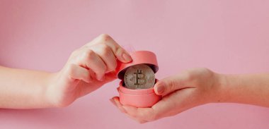 Pembe bir arka plan, sanal para simgesi pembe hediye kutusunda Bitcoin holding kadının eller.