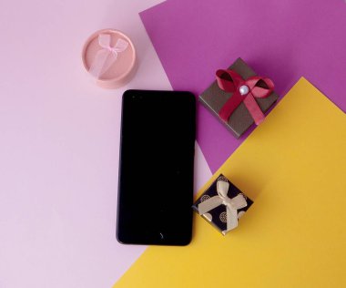 Telefon ekran ve renkli arka plan üzerinde hediyeler. En az kavramı. Düz yatıyordu. üstten görünüm. Online promosyonlar ve indirimler. Tatil hediye ve sürprizler. Hediye. Sevgililer günü. Internet Teknolojileri.