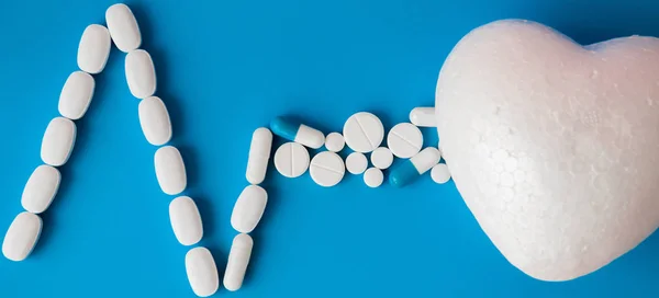 Medicines white, round heart shaped pills isolated on blue background. Tablets in the form of a line of a heart rhythm on a pastel blue background. Cardiogram of heart from pills on blue background.