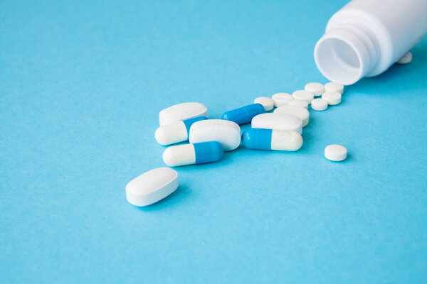 Close up pills spilling out of pill bottle on blue background. Medicine, medical insurance or pharmacy concept.