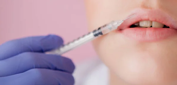 Doctor in gloves giving woman botox injections in lips, on pink background.