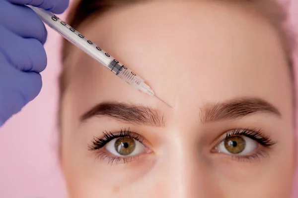 Doktor kozmetik uzmanı güzellik salonundaki genç ve güzel bir kadının cildindeki kırışıklıkları sıkmak ve düzleştirmek için yüz enjeksiyonlarını yenileme prosedürünü uyguluyor..