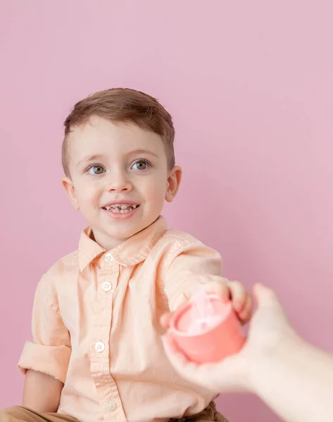 Un niño feliz con un regalo. Foto aislada sobre fondo rosa. El chico sonriente sostiene la caja presente. Concepto de vacaciones y cumpleaños — Foto de Stock