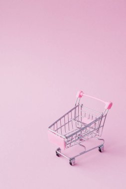 Küçük süpermarket bakkal itme sepeti oyuncak alışveriş için tekerlekler ve pembe plastik elemanları pembe pastel renkli kağıda düz arka plan yattı. Alışveriş kavramı. Kopya alanı reklam için.