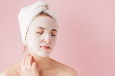Güzel genç kadın kozmetik doku maske pembe bir arka plan üzerinde bir yüzünde uyguluyor.