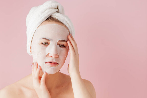Красивая молодая женщина надевает маску из косметических тканей на лицо на розовом фоне
.
