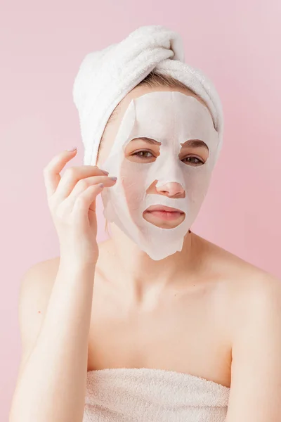 美しい若い女性はピンクの背景に顔が化粧品ティッシュ マスクを適用します — ストック写真