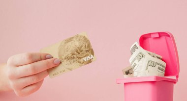 Bir kadının elinde kredi kartı ve bir çöp dolar, pembe arka plan olabilir.