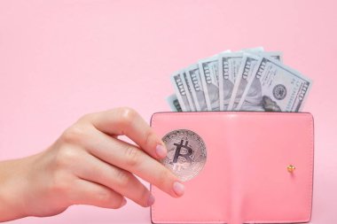Üzerinde dolar olan pembe cüzdan ve fotokopi alanı olan pembe arka planda kadının elinde bitcoin..