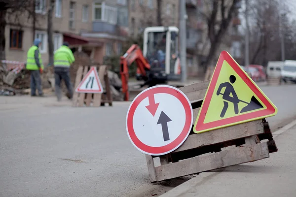 Road signs, detour, road repair on street background, truck and excavator digging hole.