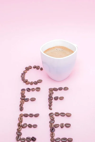 Text made of coffee beans: COFFEE. Texture of the coffee beans on a pink background. Smelly, saturated brown arabic coffee beans. Copy space.