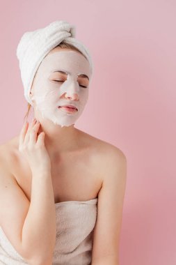 Güzel genç kadın kozmetik doku maske pembe bir arka plan üzerinde bir yüzünde uyguluyor. Sağlık ve güzellik tedavi ve teknoloji kavramı