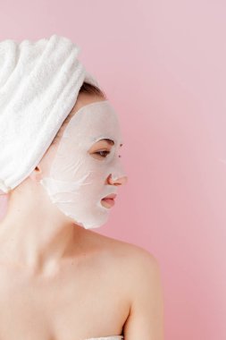 Güzel genç kadın kozmetik doku maske pembe bir arka plan üzerinde bir yüzünde uyguluyor. Sağlık ve güzellik tedavi ve teknoloji kavramı