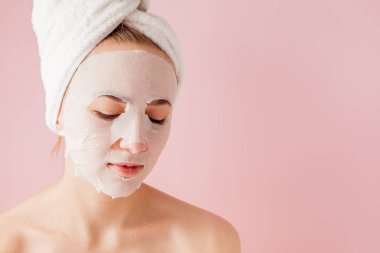 Güzel genç kadın kozmetik doku maske pembe bir arka plan üzerinde bir yüzünde uyguluyor. Sağlık ve güzellik tedavi ve teknoloji kavramı
