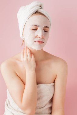 Güzel genç kadın kozmetik doku maske pembe bir arka plan üzerinde bir yüzünde uyguluyor. Sağlık ve güzellik tedavi ve teknoloji kavramı