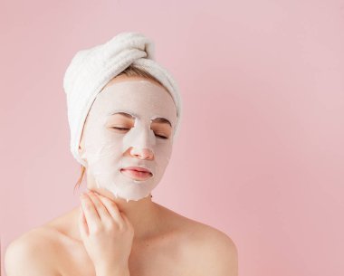 Güzel genç kadın kozmetik doku maske pembe bir arka plan üzerinde bir yüzünde uyguluyor. Sağlık ve güzellik tedavi ve teknoloji kavramı